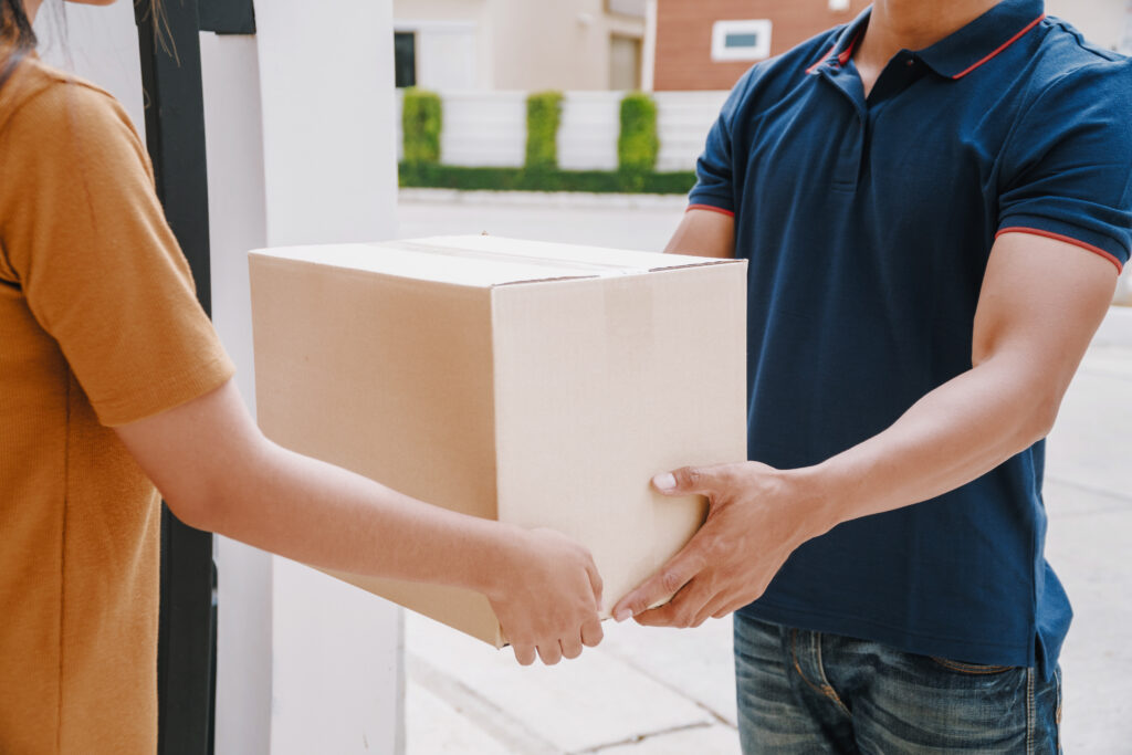 A person handing a moving box to a moving company worker standing in a doorway.