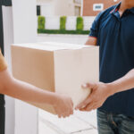 A person handing a moving box to a moving company worker standing in a doorway.